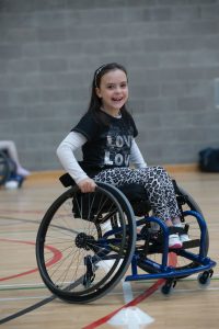 Smiling young girl playing sport in a wheelchair on an indoor court
